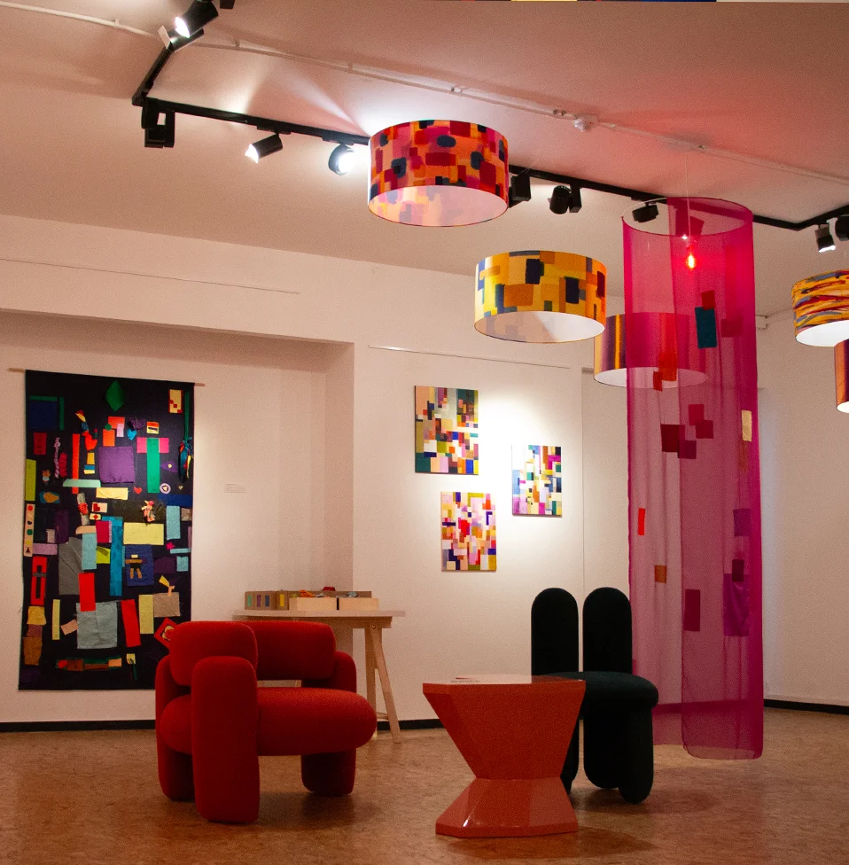 Royal Stranger red armchair displayed beside Charlotte Maubert's colorful patchwork artwork at 'La Couleur du Monde' exhibition